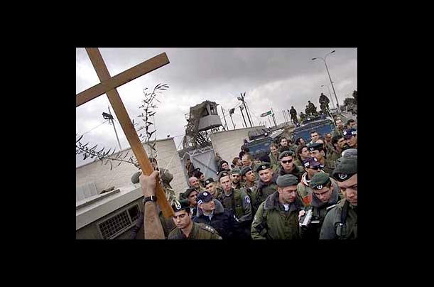 A Christian demonstrator lifts up a wooden cross as Israeli border police officers and soldiers form a barricade at the checkpoint