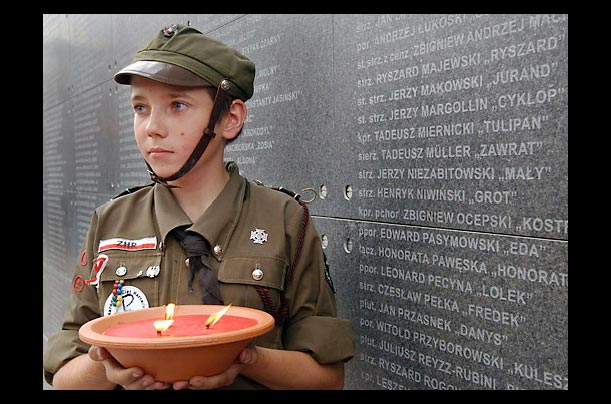 a child scout in front of a wall bearing the names of dead insurgets at the warsaw uprising museum in germany