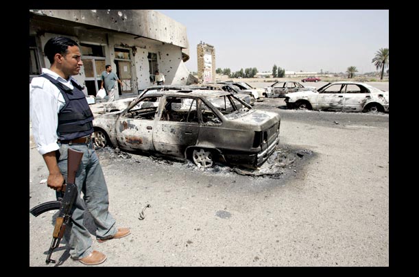iraqi policement stand next to destroyed cars after clashes between insurgents and iraqi forces in baghdad