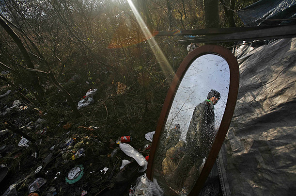 An illegal immigrant is seen reflected in a mirror outside a makeshift hut in the woods where he and other immigrants camp, near the harbor of Calais, northern France.

