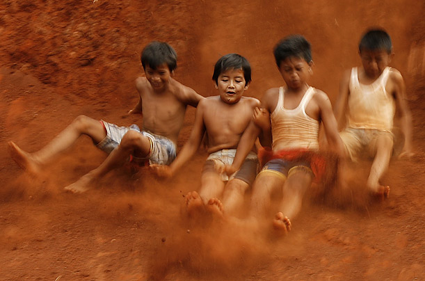 Children slide down a slope at a building foundation site as they play during their Christmas holiday in Jakarta