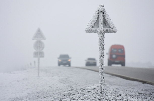 Vehicles drive past vegetation and road signs covered with hoarfrost in Almaty, Kazakhstan.

