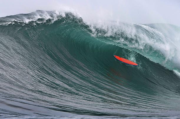 The board of a big wave surfer is engulfed by a wave as he swims under it at an offshore reef known as 