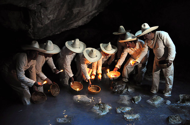Indigenous Zoque men carry baskets containing flowers and candles as offerings inside the cave of Villa Luz, during a ritual called 
