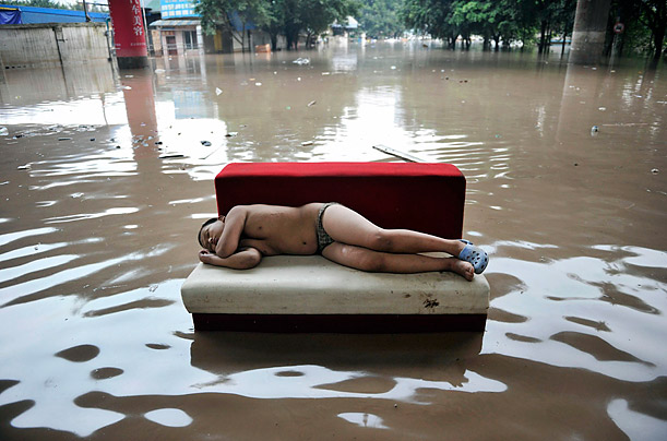 A child sleeps atop a couch on a flooded street in Chongqing, China. Torrential rain has flooded South-east China for weeks.