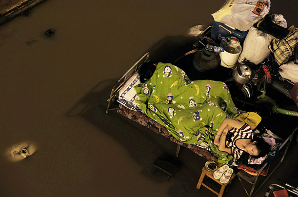  woman sleeps outdoors in the parking lot of a freight yard submerged by floods, near where the Yangtze River and Hanjiang River converge in Wuhan of Hubei Province, central China. 
