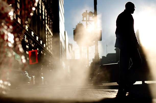 A person passes through morning sunlight shining through vented steam in a sidewalk in Philadelphia.