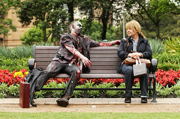 A man dressed as a zombie sits next to a woman on a park bench during the Sydney Zombie Walk. Participants dressed as the 