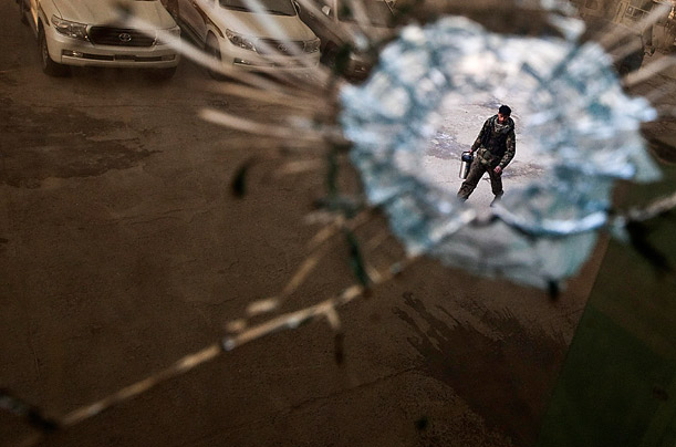 A bullet hole in a window frames a security guard outside an office building  hit during a raid by NATO forces in Kabul.
