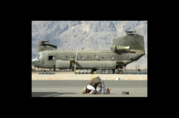 An Afghan worker prays in front of an unassembled U.S. Army Chinook helicopter at the military airbase in Kandahar, Afghanistan