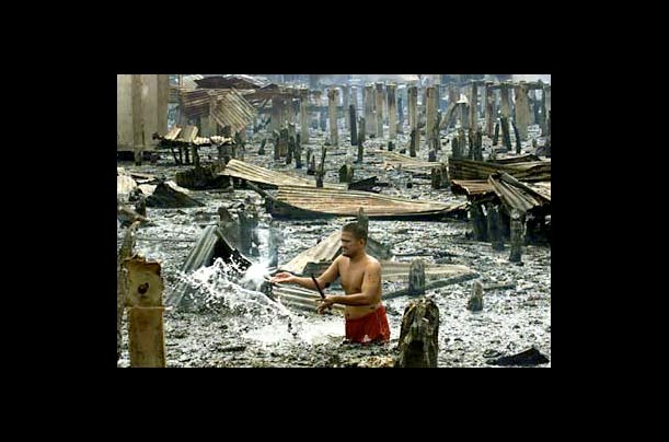 A resident douses a still-smoldering stilt following an early morning fire which gutted a coastal neighborhood in Isabela, Philippines