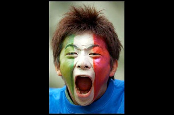 An enthusiastic soccer fan [EN] his face painted in the colors of the Italian flag [EN] screams during the Italy vs. Vegalta Sendai game