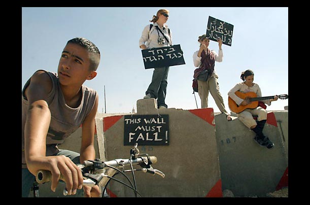 a palestinian looks on as women hold up banners to protest israel's security barier around the west bank and arab east jerusalem