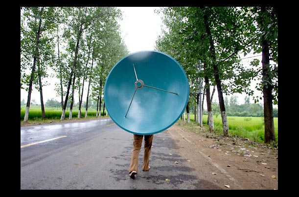 A Chinese woman carries a TV satellite dish on her back in the countryside of Jinzhai county in CHina's central province of Anhui