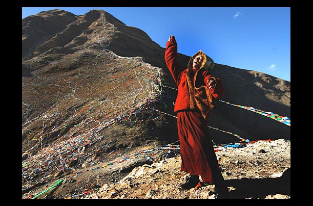 A Tibetan man prays near Prayer Flags for Tibetan New York of the Wood Bird on a mountain in Lhasa, Tibet