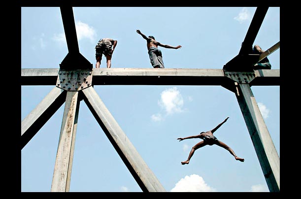 Boys dive from a 30 foot bridge into the river in kamrangir char, bangladesh
