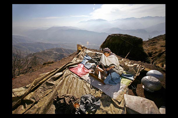 A Kashmiri earthquake survivor sews up winter clothes outside her shelter in the mountainous Buttlian area