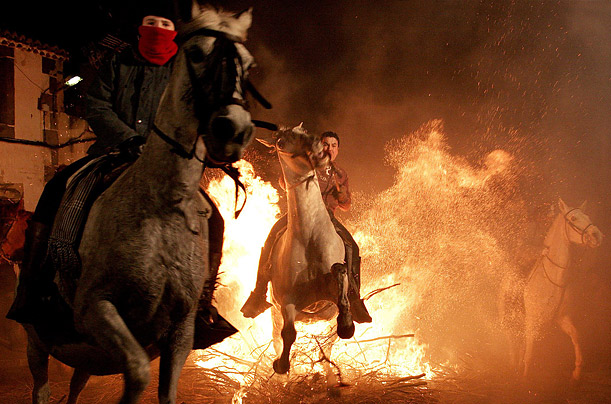 Men ride horses through flames during a purification ritual at an annual religious celebration on the night before a holiday devoted to Saint Anthony, the patron saint  of animals