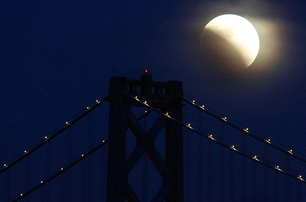 The moon is seen partially eclipsed as it rises over the San Francisco Bay Bridge in California.