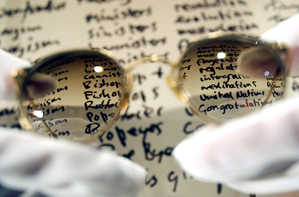 A Christie's auction house staff member holds John Lennon's tinted prescription glasses in front of his handwritten lyrics for 'Give Peace A Chance' at the Hard Rock Cafe in London, England