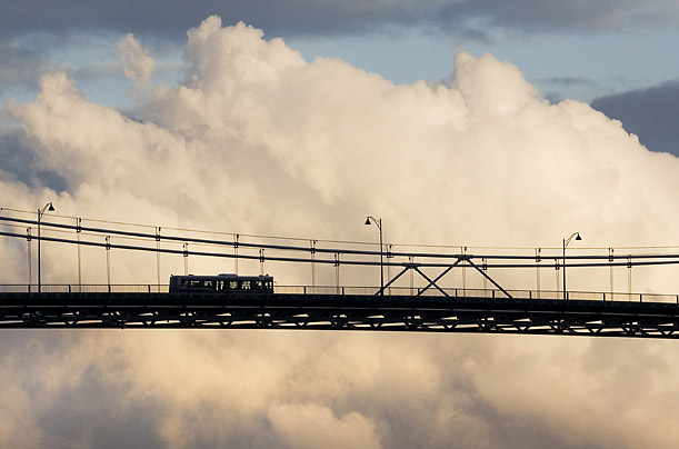 city transit bus is silhouetted against evening clouds as it crosses the Lions Gate Bridge into downtown Vancouver, British Columbia