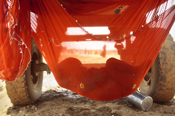 A hammock tied under a water tanker gives shade and rest to a young child whose parents work at a road construction site in Gurgaon, India.