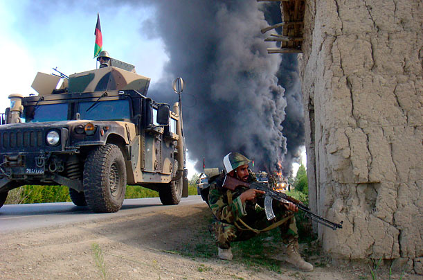 An Afghan soldier helps secure a location as trucks carrying supplies to coalition forces burn. Hundreds of people blocked a main road and set vehicles on fire to protest what they said were civilian deaths